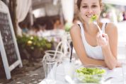 Junge Frau sitzt im Restaurant draussen und isst fröhlich einen Salat Junge Frau sitzt im Restaurant draussen und isst fröhlich einen Salat